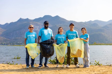 Foto de Equipo de jóvenes y grupos de trabajadores voluntarios de diversidad disfrutan de trabajo social caritativo al aire libre en la limpieza de la basura y el proyecto de separación de residuos en la playa del río - Imagen libre de derechos