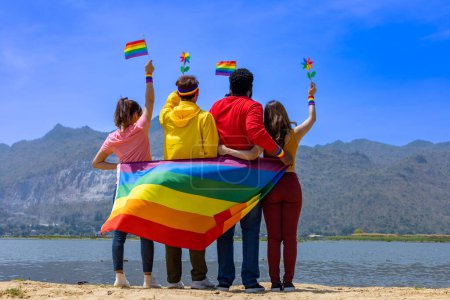 Foto de Vista posterior del grupo transgénero y fluido de género y las personas homosexuales celebrando el mes del orgullo LGBTQ + en colorido vestido y bandera del arco iris para abrazar la diferencia y la comprensión - Imagen libre de derechos