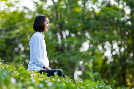 Téléchargez les photos : Femme asiatique pratique relaxant yoga méditation dans la forêt pleine de fleurs sauvages en été pour atteindre le bonheur de la paix intérieure sagesse avec la lumière du matin pour un esprit sain et l'âme - en image libre de droit