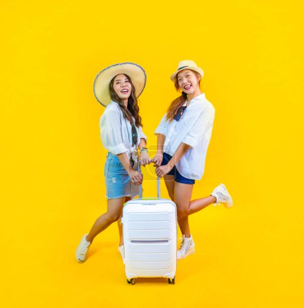 Téléchargez les photos : Deux jolies femmes asiatiques passager à la mode est excitant d'embarquer tout en portant son sac à bagages dans le bonheur pour voyage amical et vacances d'été isolé sur le fond jaune - en image libre de droit