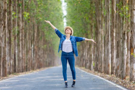 Téléchargez les photos : Femme touristique asiatique saute et danse tout en ayant des vacances au parc national tout en marchant sur la route avec colonne d'arbre pour Voyage et concept d'aventure - en image libre de droit