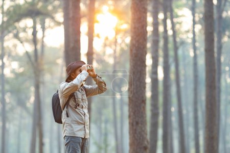 Photo for Bird watcher is looking through binoculars while exploring in the pine forest for surveying and discovering the rare biological diversity and ecologist on the field study - Royalty Free Image