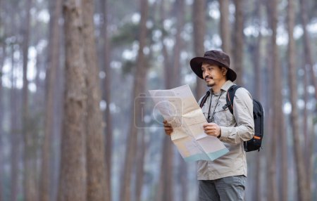 Foto de Naturalista asiático mirando el mapa en busca de dirección mientras explora la vida silvestre en el bosque de pinos para estudiar y descubrir la rara diversidad biológica y ecologista en el estudio de campo - Imagen libre de derechos