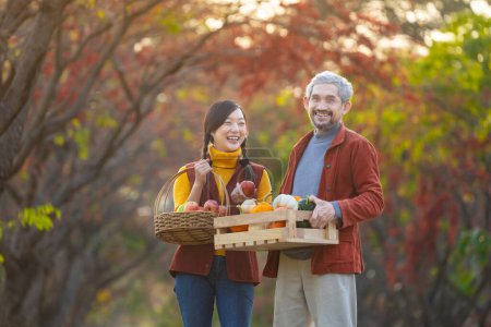 Téléchargez les photos : Famille d'agriculteurs heureux portant récolte de produits biologiques cultivés à la maison pomme, courge et citrouille avec la couleur d'automne de l'érable pendant la saison d'automne - en image libre de droit