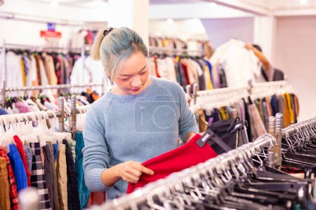 Téléchargez les photos : Femme asiatique élégante choisit pull d'occasion de la boutique de vêtements pour la mode de la saison d'hiver pour garder au chaud à la nouvelle année et vacances de Noël - en image libre de droit