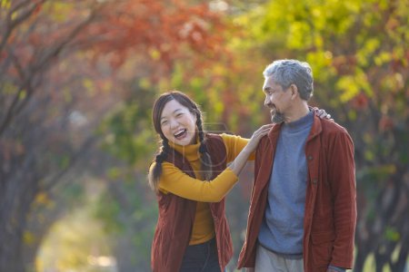 Téléchargez les photos : Heureuse famille asiatique marchant ensemble dans le parc public pendant avec la couleur d'automne de l'érable et le ginkgo pendant la saison d'automne - en image libre de droit