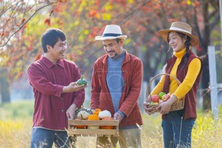 Photo for Happy Asian farmer family carrying produce harvest with homegrown organics apple, squash and pumpkin with fall color from maple tree during autumn season - Royalty Free Image