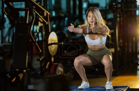 Foto de Mujer asiática con forma firme fuerte y muscular está entrenando en el día de la pierna haciendo sentadilla de salto anticipado para el muslo y el músculo de la pantorrilla en el gimnasio para una fuerza de peso corporal más baja saludable y fuerte - Imagen libre de derechos