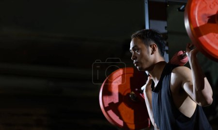 Foto de El hombre asiático del deporte muscular es entrenamiento de peso de la práctica en la barra del deadlift para el músculo de la base dentro del gimnasio con fondo oscuro para el ejercicio y el entrenamiento - Imagen libre de derechos