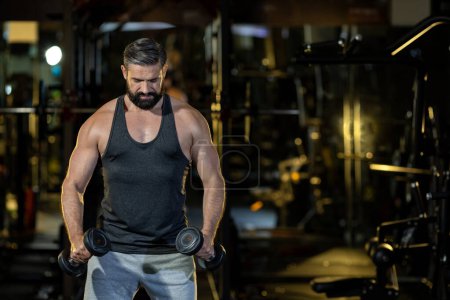Photo for Caucasian beard muscular sport man is practice weight training on double dumbbells for biceps and triceps muscle inside gym with dark background for exercising and workout usage - Royalty Free Image