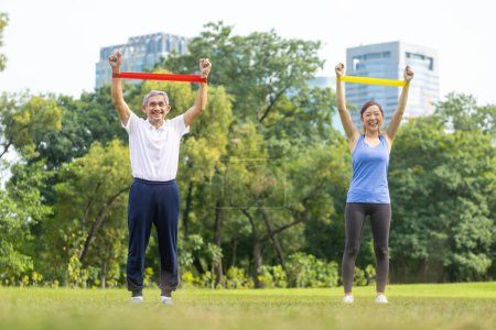 Photo for Senior asian man and his daughter are using sport rubber band to build up his arm muscle strength  in the public park for elder longevity exercise and outdoor workout usage - Royalty Free Image