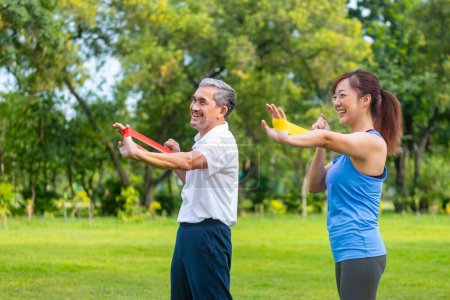 Foto de Hombre asiático mayor y su hija están utilizando banda de goma deportiva para aumentar la fuerza muscular de su brazo en el parque público para el ejercicio de longevidad mayor y el concepto de entrenamiento al aire libre - Imagen libre de derechos