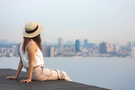 Photo for Pretty tourist woman is relaxing and enjoying her rooftop swimming pool view with cityscape background for vacation and travel concept - Royalty Free Image