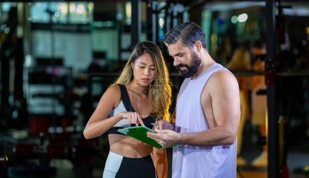 Photo for Gym customer is getting advice and suggestion from her personal trainer for exercising plan program and getting her evaluation chart from sample blood test for her workout progress concept - Royalty Free Image