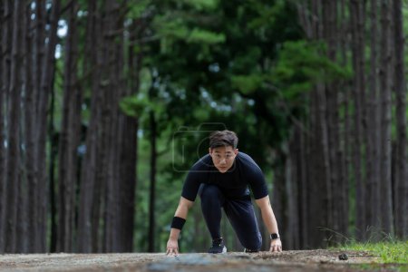 Téléchargez les photos : Chemin asiatique coureur court en plein air dans la forêt de pins chemin de terre pour l'exercice et l'entraînement des activités tout en se concentrant sur la position de départ pour la course pour un mode de vie sain et concept de remise en forme - en image libre de droit