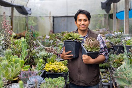 Foto de Jardinero asiático está trabajando dentro del invernadero lleno de plantas suculentas colección mientras sostiene una olla saludable para jardín ornamental y ocio hobby concepto - Imagen libre de derechos