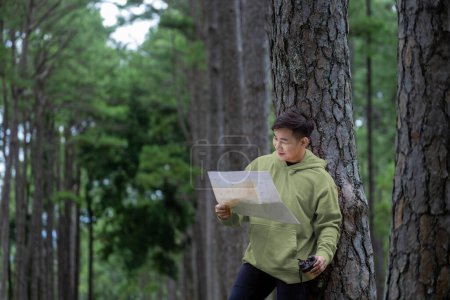 Foto de Naturalista asiático mirando el mapa en busca de dirección mientras explora la vida silvestre en el bosque de pinos para estudiar y descubrir la rara diversidad biológica y ecologista en el estudio de campo - Imagen libre de derechos