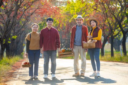 Photo for Happy Asian farmer family with senior parent are carrying produce harvest with homegrown organics apple, squash and pumpkin with fall color from maple tree during autumn season for agriculture - Royalty Free Image