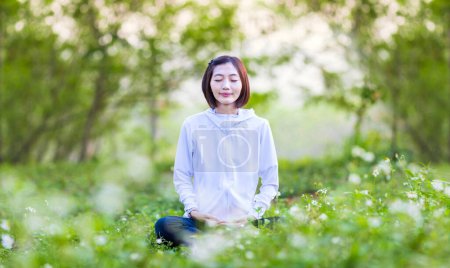 Téléchargez les photos : Femme asiatique pratique relaxant yoga méditation dans la forêt pleine de fleurs de marguerite en été pour atteindre le bonheur de la paix intérieure sagesse avec la lumière du matin pour un esprit sain et l'âme - en image libre de droit