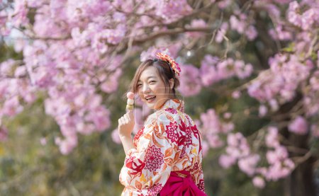 Photo for Japanese woman in traditional kimono dress holding sweet hanami dango dessert while walking in the park at cherry blossom tree during spring sakura festival - Royalty Free Image