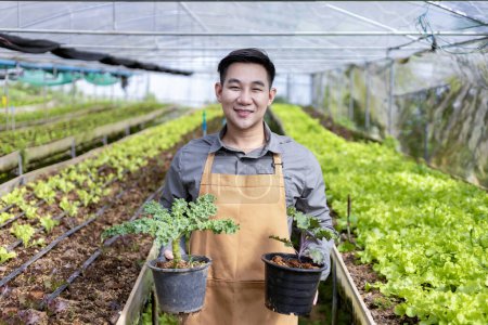 Foto de Retrato de granjero local asiático cultivando lechuga de ensalada en invernadero usando enfoque de suelo orgánico para negocio propio familiar y recogiendo algunos para la venta - Imagen libre de derechos