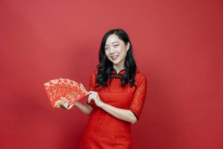 Téléchargez les photos : Femme asiatique tenant enveloppe fortune argent rouge bénédiction mot chinois qui signifie "Puissiez-vous avoir une grande chance et un grand profit" isolé sur fond rouge pour le Nouvel An chinois - en image libre de droit