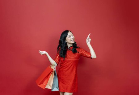 Photo for Asian chinese woman with red cheongsam or qipao holding shopping bag wish the good luck sale and prosperity in Chinese New Year celebration holiday isolated on the red background - Royalty Free Image
