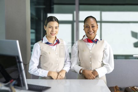 Téléchargez les photos : Équipe d'agents de bord de la diversité posant avec le sourire au comptoir d'enregistrement avant l'embarquement pour accueillir les passagers à bord pour le service aérien et le concept de transport aérien - en image libre de droit