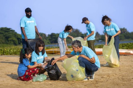 Téléchargez les photos : Une équipe de jeunes travailleurs bénévoles de la diversité profitent du travail social de bienfaisance en plein air pour nettoyer les ordures et le projet de séparation des déchets à la plage de la rivière - en image libre de droit