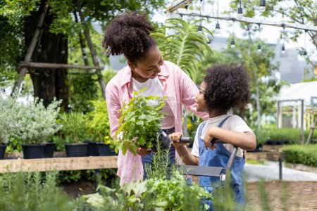 Téléchargez les photos : La mère et la fille africaines choisissent des plantes potagères et herbacées de la pépinière du centre de jardin local avec un panier rempli de plantes d'été pour le jardinage de week-end et en plein air - en image libre de droit