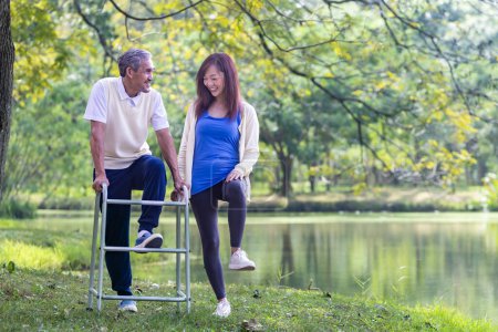 Téléchargez les photos : Homme âgé asiatique avec marcheur et sa fille marchant ensemble dans le parc faire de l'exercice léger et la thérapie physique pour le renforcement musculaire dans la longévité et un mode de vie sain après la retraite concept - en image libre de droit