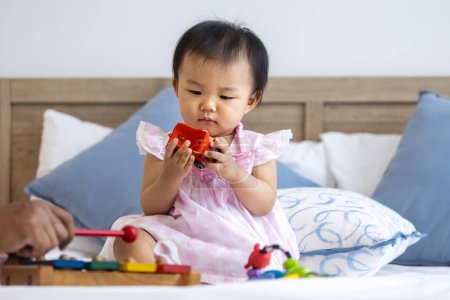 Photo for Adorable little asian baby toddler is sitting on the bed playing wooden melody toy for preschool learning and growth development - Royalty Free Image