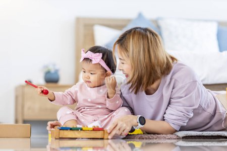 Téléchargez les photos : Mère asiatique joue avec sa jolie fille bébé souriante avec bloc jouet en bois tout en passant du temps de qualité dans le lit pour le bonheur de la famille et l'utilisation parentale - en image libre de droit