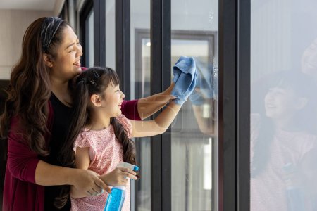 Téléchargez les photos : Mère et fille asiatiques s'aident mutuellement à nettoyer la maison en essuyant la fenêtre en verre clair pour les tâches quotidiennes de routine et l'entretien ménager - en image libre de droit