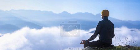 Téléchargez les photos : Panorama vue arrière de l'homme est relaxant pratiquant la méditation yoga mudra au sommet de la montagne avec de la brume et du brouillard en été pour atteindre le bonheur de la paix intérieure sagesse pour l'esprit sain et l'âme - en image libre de droit