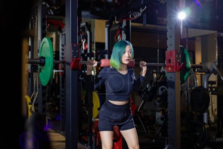 Foto de Mujer deportiva muscular asiática es la práctica de entrenamiento con pesas en la barra de levantamiento de pesas para el músculo del núcleo dentro del gimnasio con fondo oscuro para el ejercicio y el entrenamiento - Imagen libre de derechos