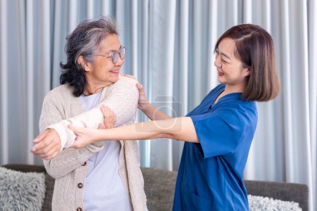 Téléchargez les photos : Femme asiatique âgée a obtenu la visite des services médicaux de l'infirmière soignante à la maison tout en faisant de la physiothérapie à l'épaule étirement pour la douleur musculaire dans les soins de santé et le bien-être des pensions - en image libre de droit