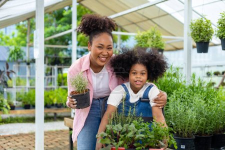 Téléchargez les photos : La mère et la fille africaines choisissent des plantes potagères et herbacées de la pépinière du centre de jardin local avec un panier rempli de plantes d'été pour le jardinage de week-end et l'extérieur - en image libre de droit