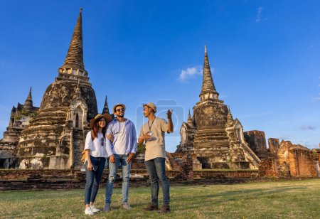 Foto de Guía turístico local tailandés está explicando la historia de la antigua Siam a la pareja de turistas en su viaje de luna de miel mochilero al antiguo templo de Ayutthaya, Tailandia - Imagen libre de derechos