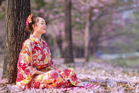 Japanese woman wearing kimono dress is doing meditation under sakura tree during cherry blossoming season for inner peace, mindfulness and zen practice