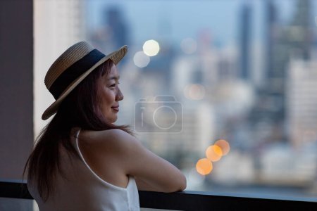 Asiatische Touristin genießt ihre Stadtsilhouette vom Hotelzimmerbalkon aus für Urlaub und Reise