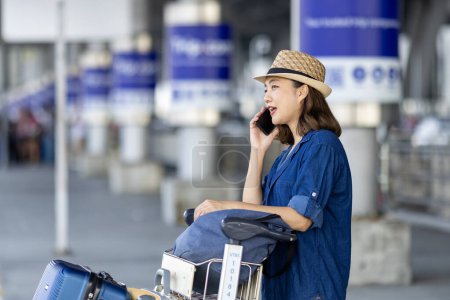 Photo for Asian woman tourist passenger is using mobile application to call pick up taxi at airport terminal for transportation during her vacation travel and long weekend holiday - Royalty Free Image