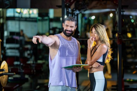 Photo for Gym customer is getting advice and suggestion from her personal trainer for exercising plan program and getting her evaluation chart from sample blood test for her workout progress - Royalty Free Image