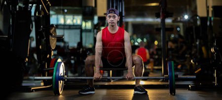 Téléchargez les photos : Asiatique musclé sport homme est la pratique de musculation sur haltère haltère pour le muscle de base à l'intérieur de la salle de gym avec fond sombre pour l'exercice et l'entraînement - en image libre de droit