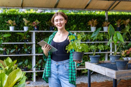 Téléchargez les photos : Jardinier caucasien choisit des plantes d'alocasie à l'intérieur de la serre pour la forêt tropicale plante tendre exotique pour le jardinage ornemental - en image libre de droit