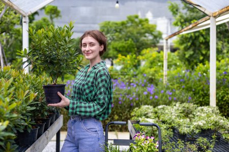Téléchargez les photos : Jeune client caucasien choisit une plante exotique de la pépinière du centre de jardin local avec un panier plein de plantes d'été pour le jardinage de week-end et en plein air - en image libre de droit