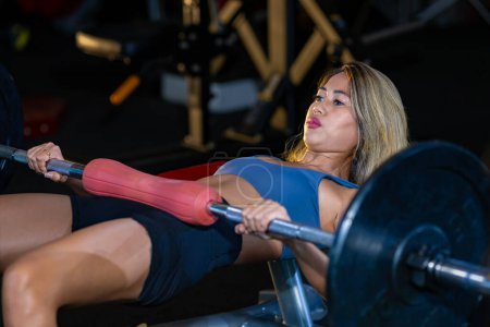 Foto de Mujer asiática es la práctica de levantamiento de peso en la barra para el músculo del núcleo dentro del gimnasio con fondo oscuro para el ejercicio y el entrenamiento - Imagen libre de derechos