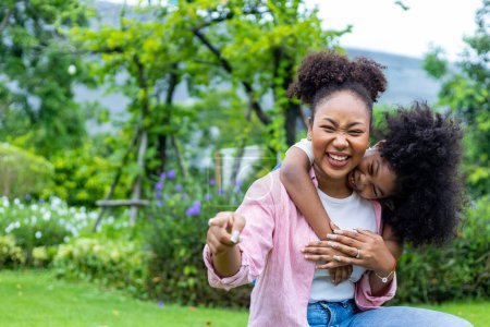 Photo for African American mother is playing piggyback riding with her young daughter while having summer picnic in the public park for wellbeing and happiness - Royalty Free Image