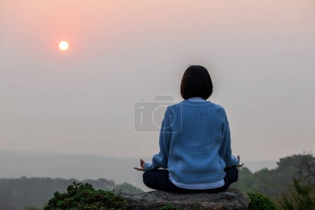 Téléchargez les photos : Vue arrière de la femme pratique relaxante méditation yoga mudra sur le sommet de la montagne avec lever du soleil pendant l'été pour atteindre le bonheur de la paix intérieure sagesse pour un esprit sain et l'âme - en image libre de droit