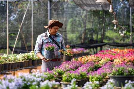 Téléchargez les photos : Jeune jardinier asiatique choisit plante à fleurs de la pépinière du centre de jardin local plein de plantes d'été pour le jardinage week-end et le concept de passe-temps en plein air - en image libre de droit